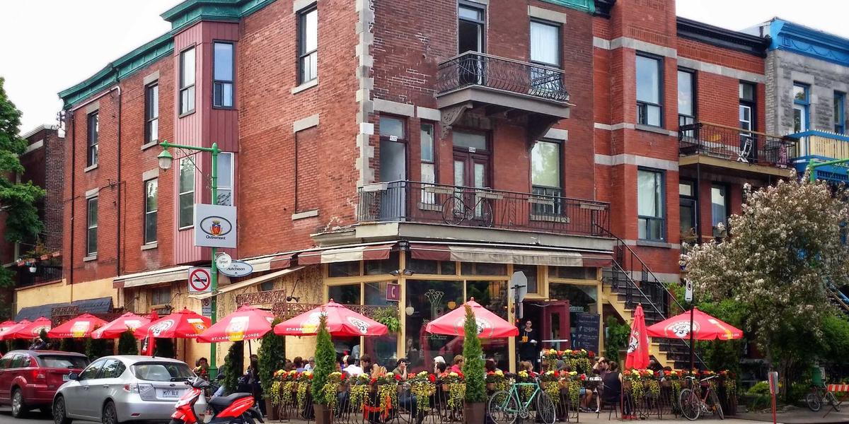 A neighbourhood street with red-brick buildings and cafe umbrellas — local is a place, not a compromise