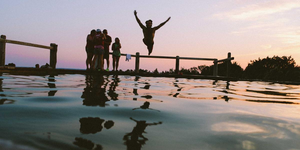Friends jumping joyfully on a seaside pier at sunset — the volunteer community energy behind open source