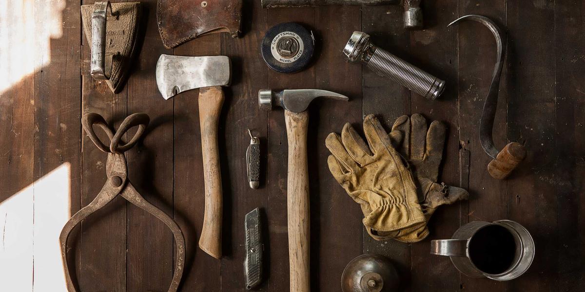 A flat-lay of well-worn hand tools on wood — instruments anyone may pick up, inspect and repair